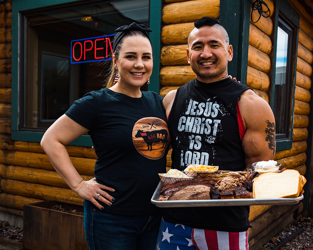 Stephen and Taylor Kina smiling and holding a tray of BBQ.