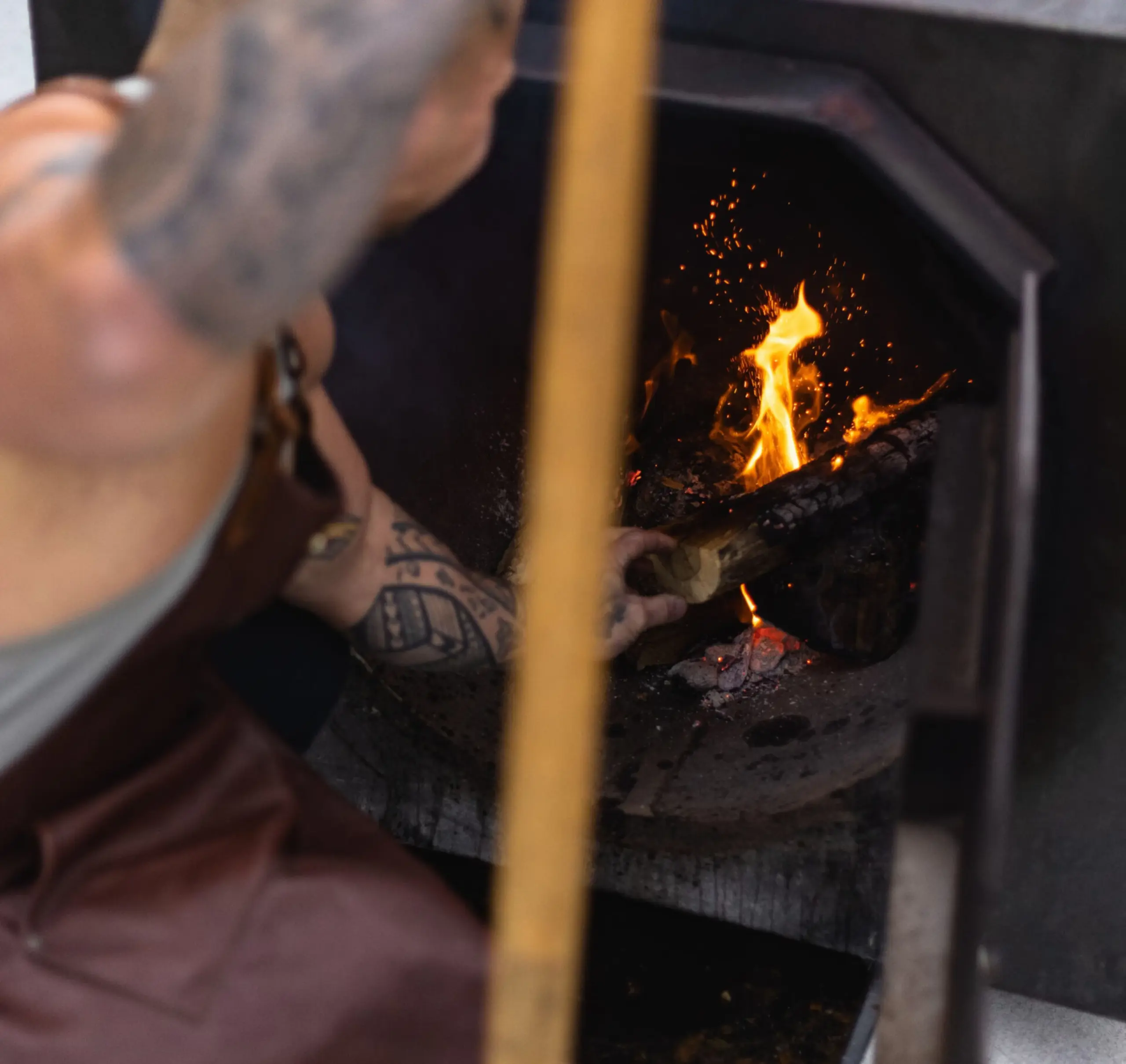 Pitmaster Stephen Kina is adjusting wood in smoker via open fire door